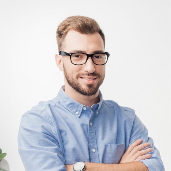 Portrait d'un homme souriant avec des lunettes, portant une chemise bleue, dans un environnement lumineux.