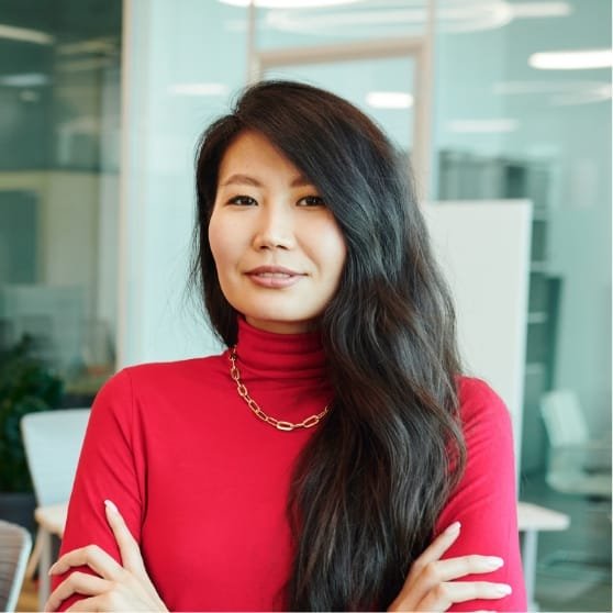 Portrait d'une femme en chemise rouge avec un collier doré, dans un environnement de bureau lumineux
