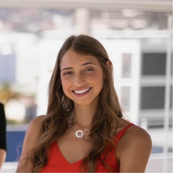 Portrait d'une femme souriante portant un haut rouge et un collier, dans un environnement lumineux.